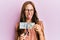 Young brunette woman cutting dollars with scissors for currency devaluation sticking tongue out happy with funny expression