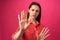 Young brunette woman does stop sign with palm against pink background