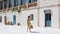 Young brunette woman in dress with sunflowers and yellow handbag walking along empty street in historical and resort part of the c