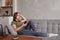 Young brunette woman enjoying the music in wireless headphones connected to smartphone, lying on couch at home alone