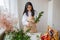 a young brunette woman florist in apron cuts leaves from the stems before starting to create a bouquet in her workshop