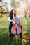 Young brunette woman with glasses playing cello at sunset in the park, on a green grass. Vertical