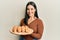 Young brunette woman holding bread looking positive and happy standing and smiling with a confident smile showing teeth