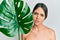 Young brunette woman holding green plant leaf close to beautiful face clueless and confused expression