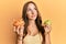 Young brunette woman holding nachos and healthy green apple smiling looking to the side and staring away thinking