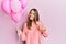 Young brunette woman holding pink balloons pointing finger to one self smiling happy and proud