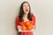 Young brunette woman holding plate with fresh oranges angry and mad screaming frustrated and furious, shouting with anger looking