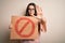 Young brunette woman holding protest banner with prohibited symbol over isolated background with open hand doing stop sign with