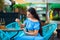 Young brunette woman with long hair in blue crop top is sitting at table in cafe and drinking from jar