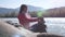 Young brunette woman putting pebble stack next to the mountain river on sunny day