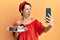 Young brunette woman with short hair holding sweets cakes taking a selfie picture angry and mad screaming frustrated and furious,