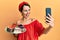 Young brunette woman with short hair holding sweets cakes taking a selfie picture smiling and laughing hard out loud because funny