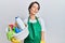 Young brunette woman with short hair wearing apron holding cleaning products looking sleepy and tired, exhausted for fatigue and