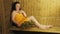 A young brunette woman is sitting in a bath with a broom wrapped in a towel