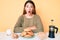 Young brunette woman sitting on the table having breakfast scared and amazed with open mouth for surprise, disbelief face