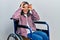 Young brunette woman sitting on wheelchair doing ok gesture like binoculars sticking tongue out, eyes looking through fingers