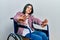 Young brunette woman sitting on wheelchair doing stop gesture with hands palms, angry and frustration expression