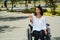 Young brunette woman sitting in wheelchair smiling with positive attitude, outdoors environment, physical recovery