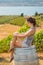 Young brunette woman sitting on a wooden wine barrel in front of a Okanagan vineyard.