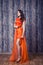 Young brunette woman in stylish orange silk dress posing on wood