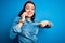 Young brunette woman talking on smartphone over blue isolated background with surprise face pointing finger to himself