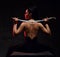 Young brunette woman warrior, martial arts fighter sits topless back to camera holding sword on shoulders, looking aside