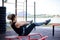 Young brunette woman, wearing black fitness overall, doing abs on horizontal bars on sports playground by city lake in summer. Fit