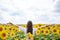 Young brunette woman, wearing boho hippie clothes, standing in the middle of yellow sunflowers field, holding wheat stalks,