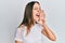 Young brunette woman wearing casual white t shirt shouting and screaming loud to side with hand on mouth