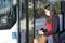 Young brunette woman wearing face mask at the bus stop while holding bag and mobile. Coronavirus