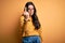 Young brunette woman wearing glasses and casual sweater over yellow isolated background Showing middle finger, impolite and rude