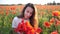 Young brunette woman in white dress stands in the middle of the field of poppies. Charming lady with incredible smile