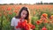 Young brunette woman in white dress stands in the middle of the field of poppies. Charming lady with incredible smile