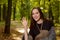 Young brunette woman in a wool poncho standing in the sun on a footpath in a Park green and waving in greeting.