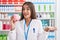 Young brunette woman working at pharmacy drugstore holding piggy bank celebrating achievement with happy smile and winner