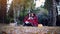 Young brunette women sitting on picnic bundled up in a blanket drinking hot tea in autumn park. Girls on a fallen leaves