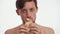 Young brutal Caucasian hungry brunette half naked man with beard stare at camera, eagerly eat with pleasure fresh sandwich in slow