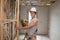 Young builder industry trainee man on his 20s wearing protective helmet learning working with drill at industrial workshop site