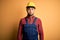Young builder man wearing construction uniform and safety helmet over yellow isolated background puffing cheeks with funny face
