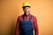 Young builder man wearing construction uniform and safety helmet over yellow isolated background sticking tongue out happy with