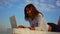 Young buisness woman working online while lying on the bench during the weekend by the sea