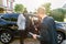 Young business couple, African man and Caucasian woman, looking for car to buy, woman sitting n the car, man standing