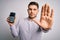 Young business man with blue eyes holding dataphone payment terminal over isolated background with open hand doing stop sign with