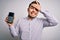 Young business man with blue eyes holding dataphone payment terminal over isolated background stressed with hand on head, shocked