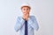 Young business man wearing contractor safety helmet over isolated background shocked covering mouth with hands for mistake