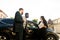 Young business people, two men, Caucasian and African, standing at the yard of car salon outdoors with young woman