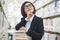 Young Business Woman Contemplating and Looking Up in Bookstore with a Stack of Books