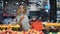Young business woman girl buyer client blonde lady consumer stands in shop near counter with fruits in grocery store