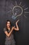 A young business woman has a great idea and raises her hands up pointing to a lightbulb on the board.