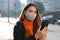 Young business woman with protective mask checking email on mobile phone waiting for a taxi on street in the morning